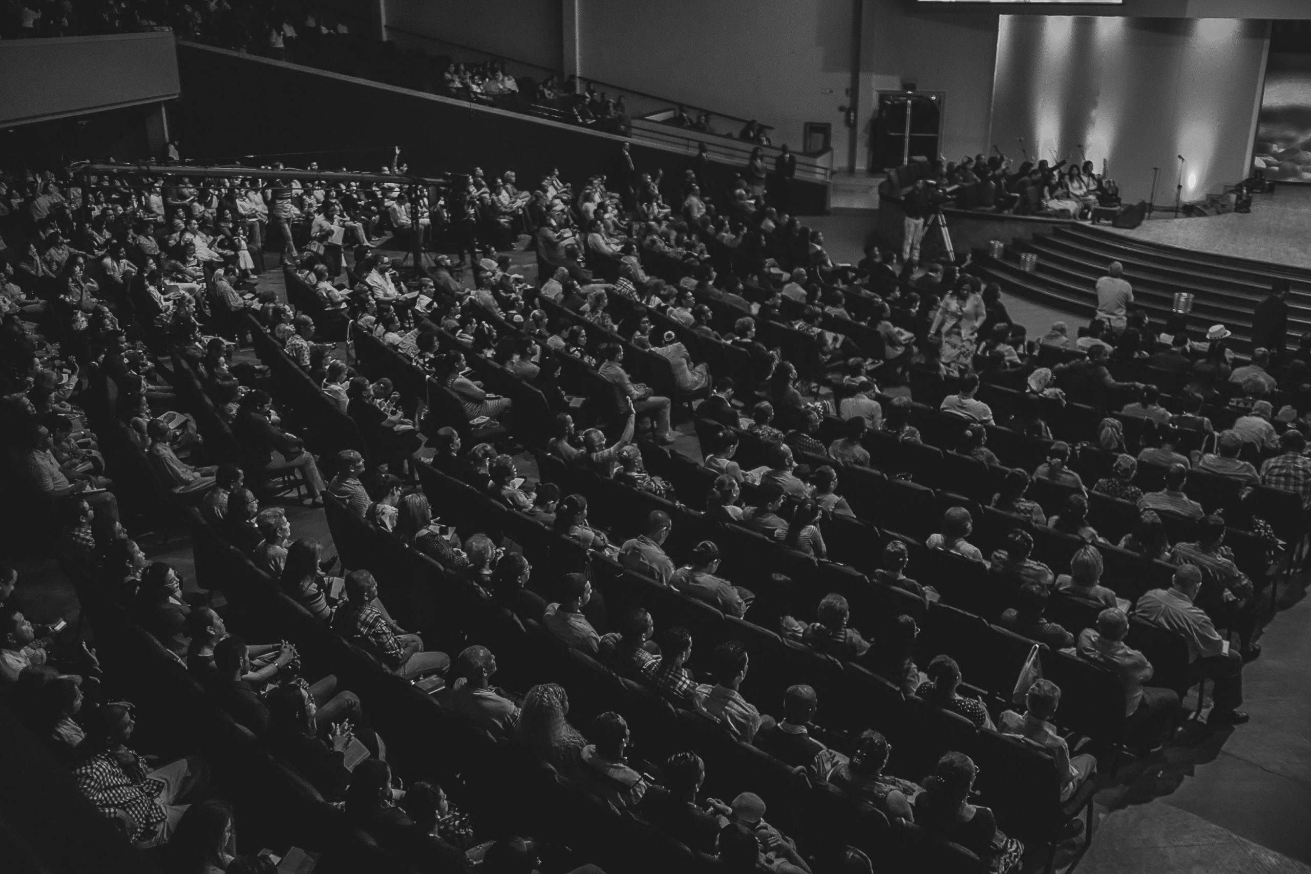 Monochrome image of a large audience seated in a theater auditorium from a high angle.